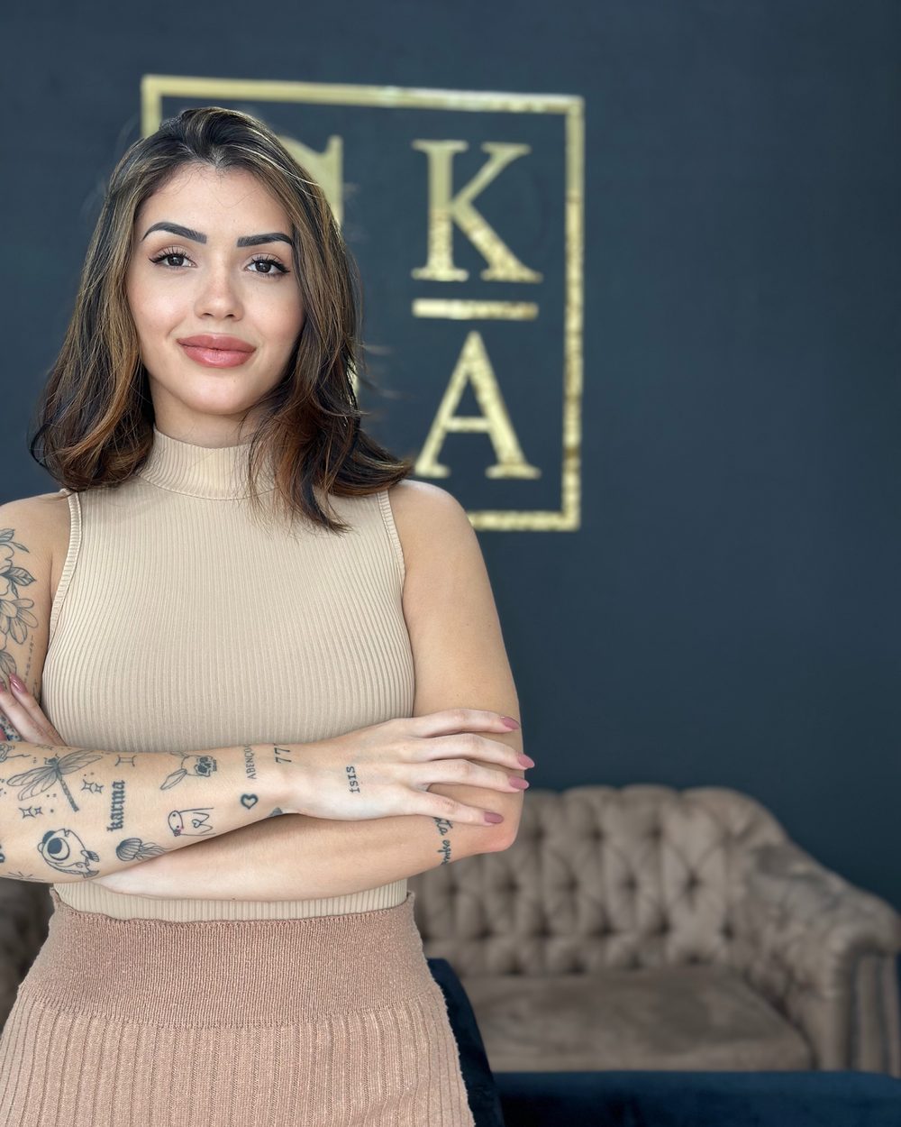 Kathleen Araújo no studio, em frente ao letreiro dourado SKA